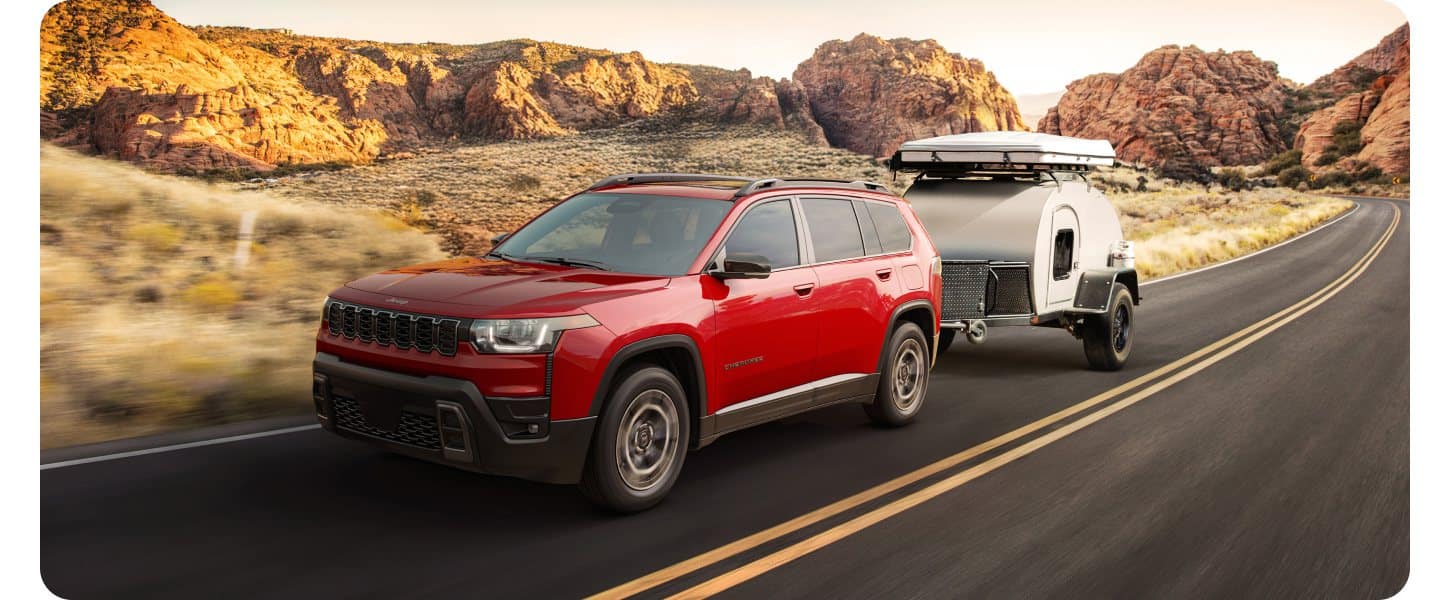A red Jeep Cherokee tows a small trailer down a southwestern road.