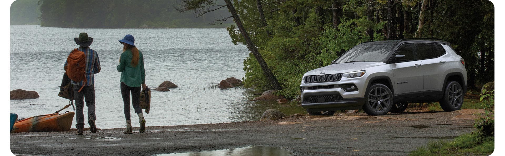 Un Jeep Compass Limited Altitude 2026 plateado estacionado junto a un lago, con una pareja cerca.