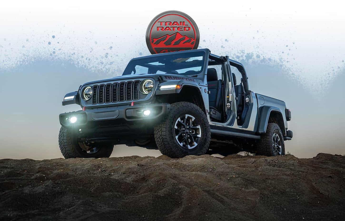 A gray 2026 Jeep Gladiator Rubicon with its doors removed, parked on the top of a rocky hill. The Trail Rated badge.