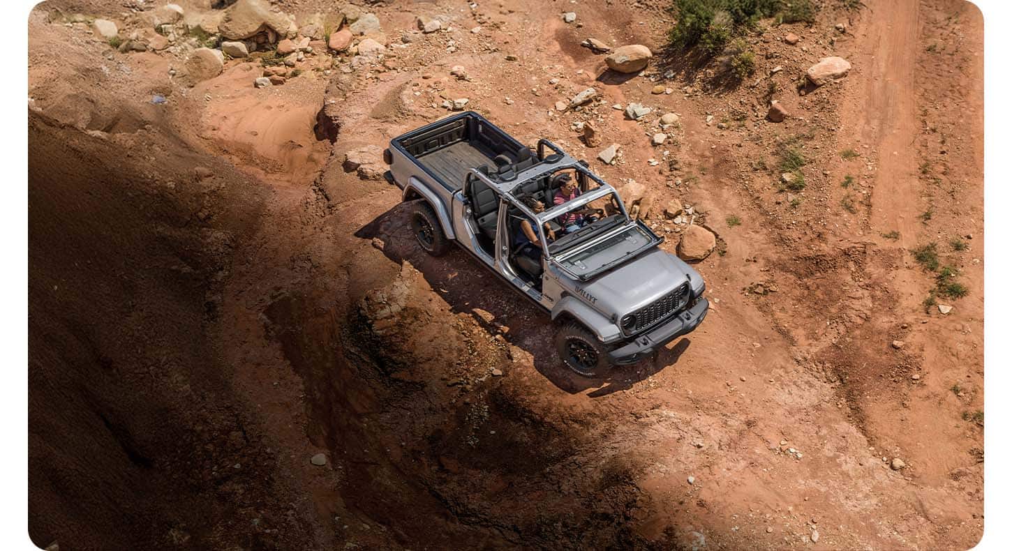 A top-down angle of a gray 2026 Jeep Willys with its doors and top removed, traveling on a rocky trail off-road.