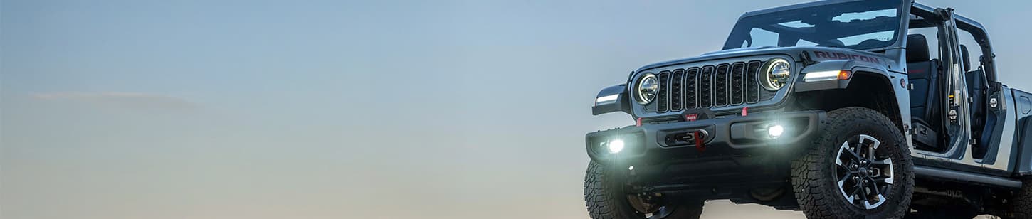 A partial driver-side front angle of a gray 2026 Jeep Gladiator Rubicon X with its doors and top removed.