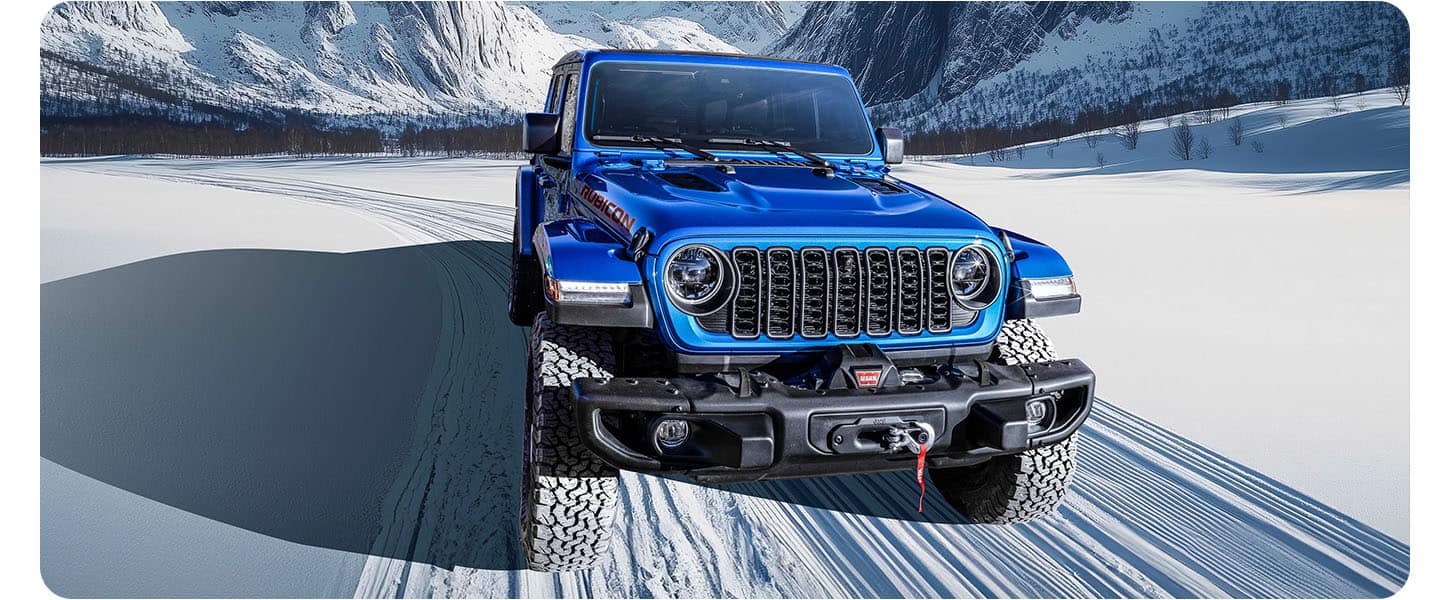 A blue 2026 Jeep Gladiator Rubicon X traveling on a snow-covered road, through the mountains.