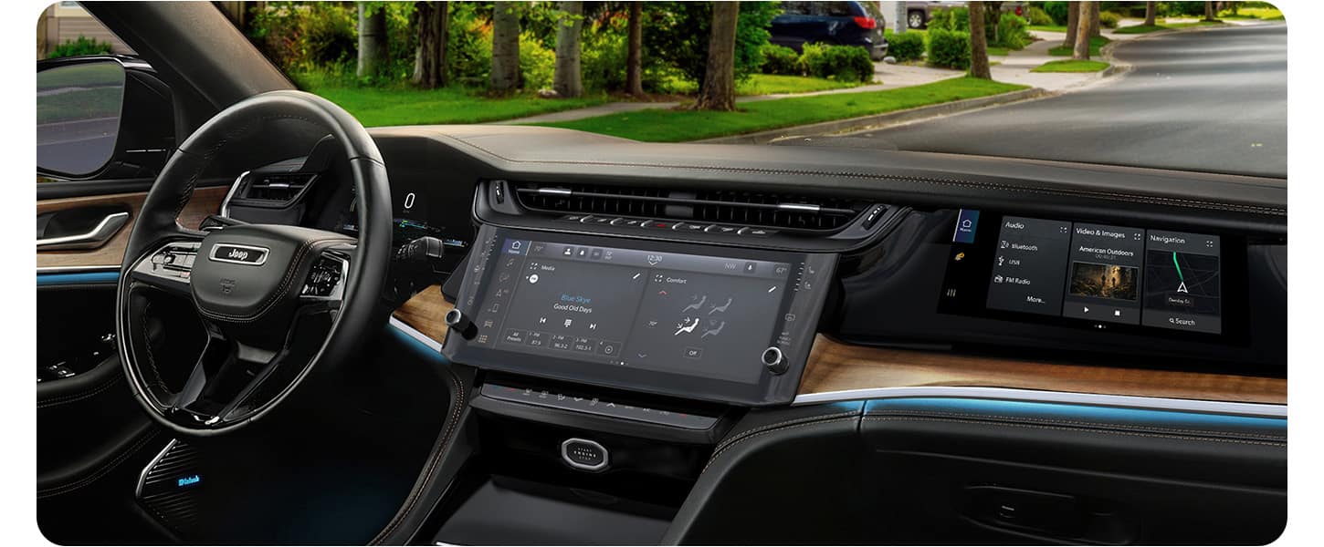 The steering wheel, Uconnect touchscreen, Front Passenger Interactive Touchscreen Display and wireless charging pad in the 2026 Jeep Grand Cherokee Summit.