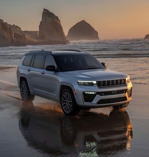 Silver 2026 Jeep Grand Cherokee Summit on a coastal shore at sunset