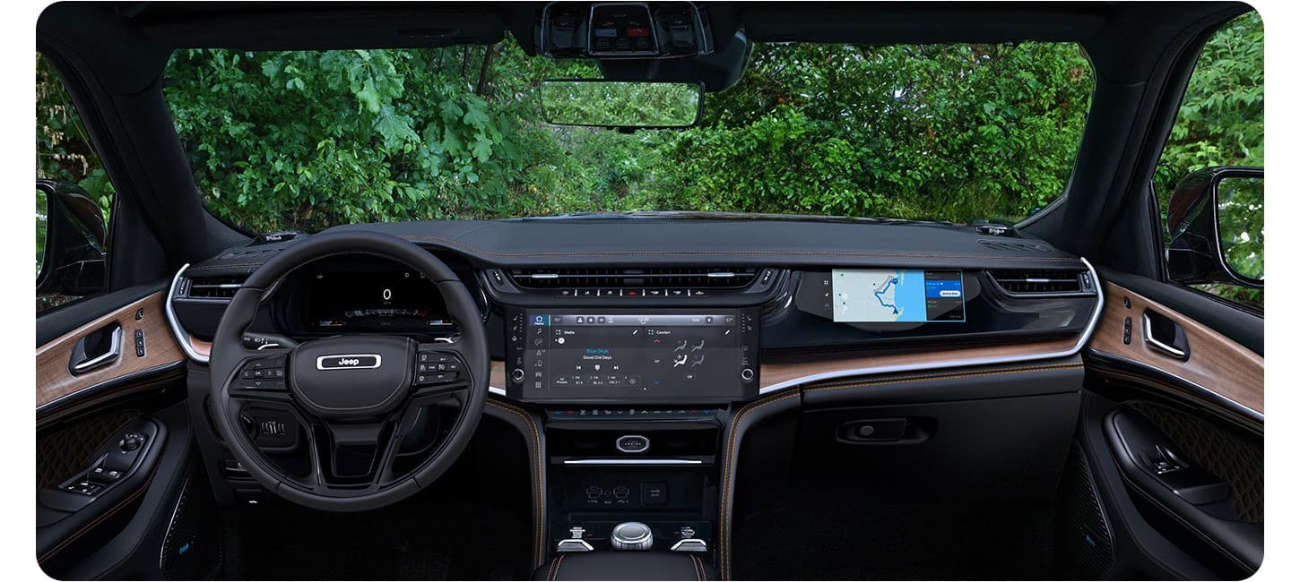 The front seat area of the 2026 Jeep Grand Cherokee Summit focusing on the steering wheel, Uconnect touchscreen and Front Passenger Interactive Display.