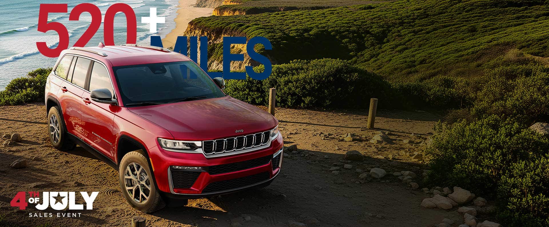 A red 2026 Jeep Grand Cherokee Limited parked on a beach near the shoreline. 520 + Miles. The 4th of July Sales Event.