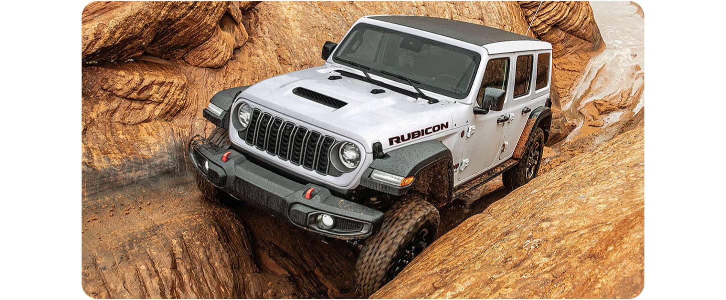 Un Jeep Wrangler Rubicon 2026 blanco trepa por una superficie rocosa a través de un paso de montaña angosto.