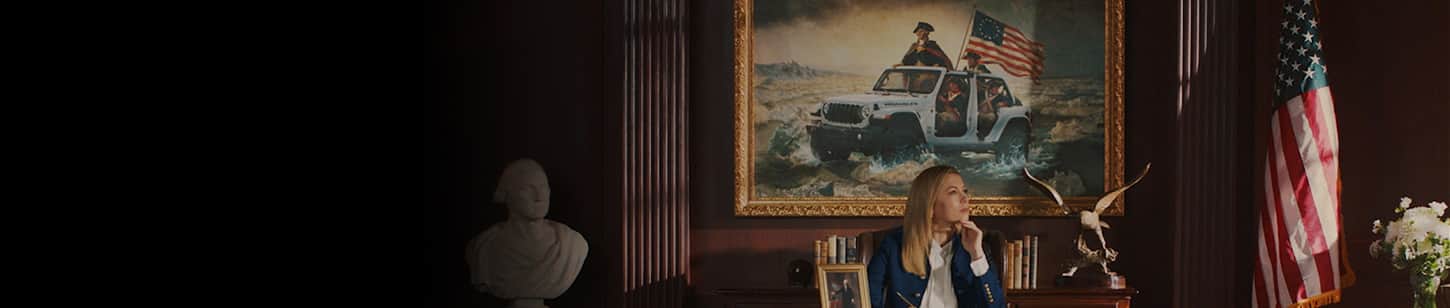 A woman at a desk in a government office with a painting behind her of George Washington with three soldiers crossing a shallow part of the Delaware River in a white Wrangler with its doors and top removed.