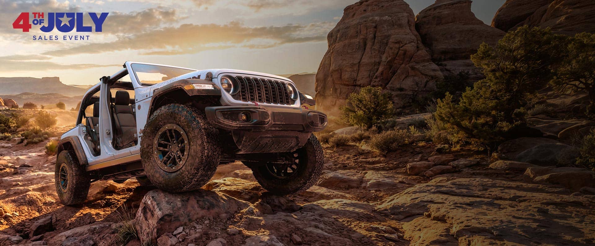 A white 2026 Jeep Wrangler Rubicon with its doors and top removed, crawling over a very rugged trail of bedrock. The 4th o July Sales Event.
