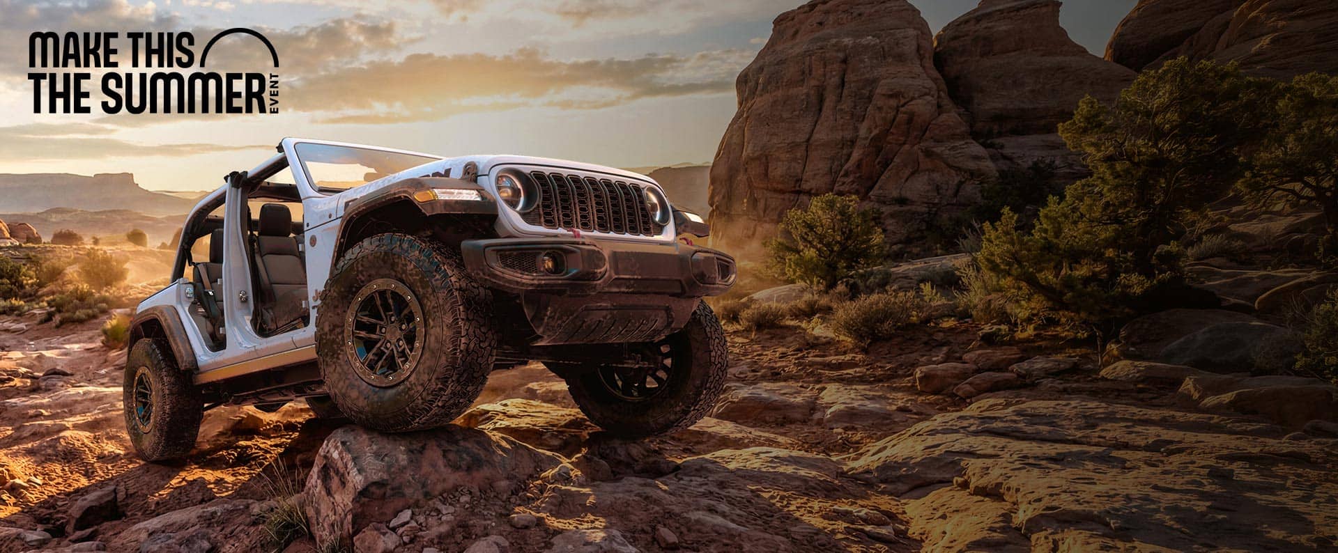 A white 2026 Jeep Wrangler Rubicon with its doors and top removed, crawling over a very rugged trail of bedrock. Make This The Summer Event.