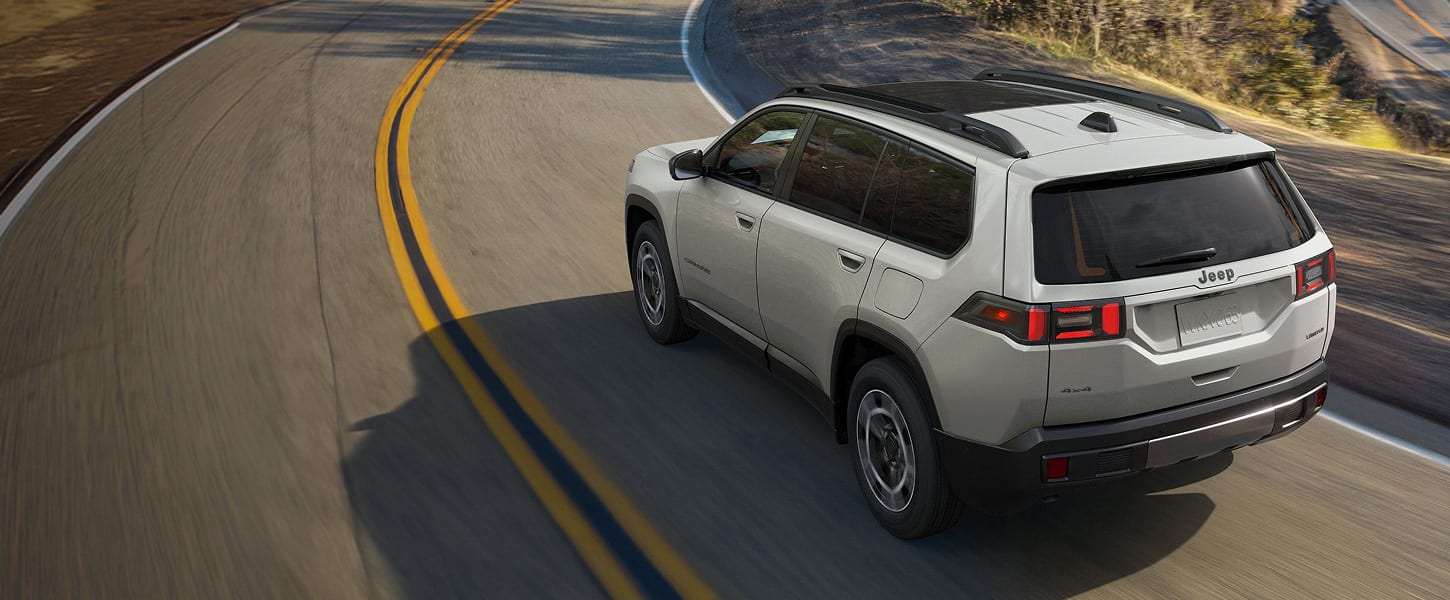 A light gray 2027 Jeep Cherokee Limited being driven down a country road.