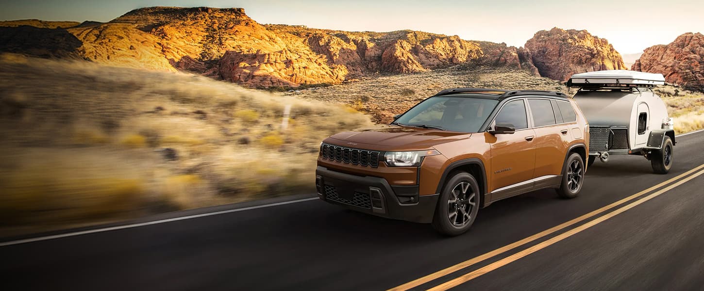 A 2027 Jeep Cherokee Overland with a Copper Shino exterior paint color being driven down a country road in the mountains.