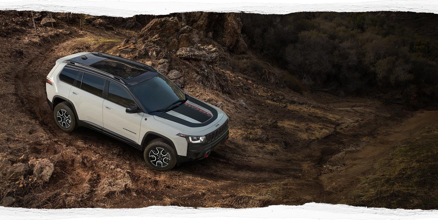 A light gray 2027 Jeep Cherokee Trailhawk descending a rocky slope.