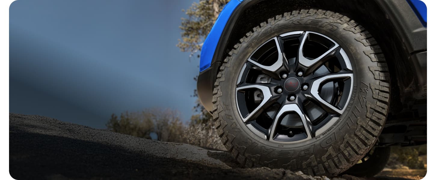 Close-up of a Falken Wildpeak All-Terrain Tire on a blue 2027 Jeep Compass Trailhawk outside during the day.