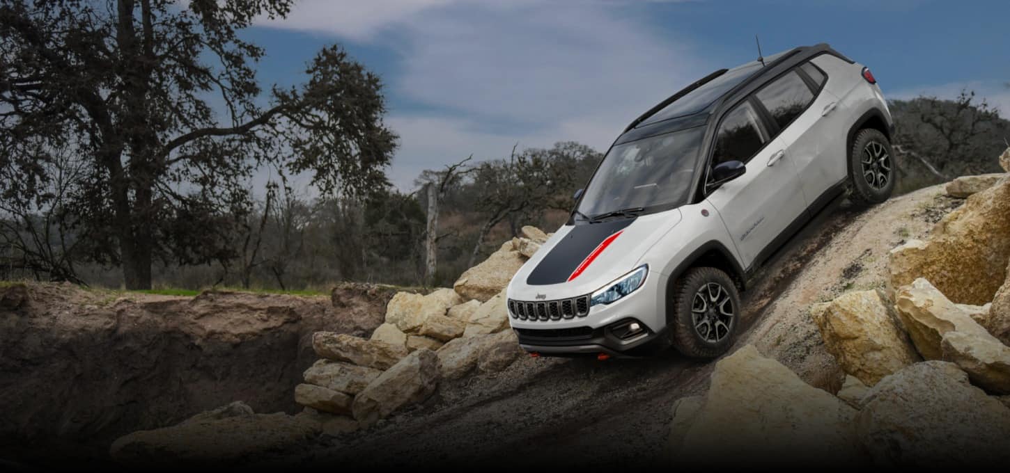 Side view of a white 2027 Jeep Compass Trailhawk being driven down a steep path with rocks on both sides.