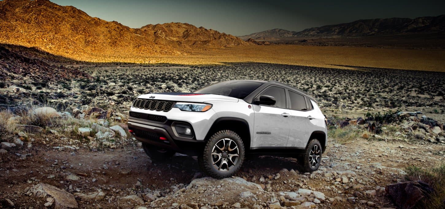 Side view of a white 2027 Jeep Compass Trailhawk being driven over a rocky trail.