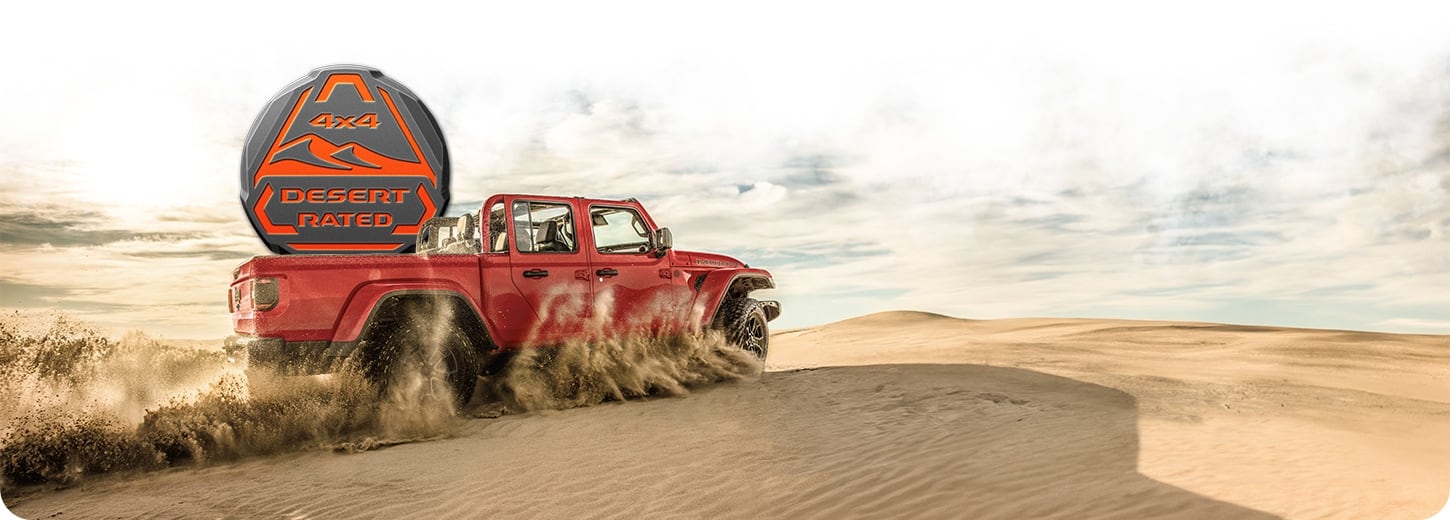 A red 2027 Jeep Gladiator Mojave X with its top off kicks up sand in the desert. The Desert Rated badge is superimposed behind it.