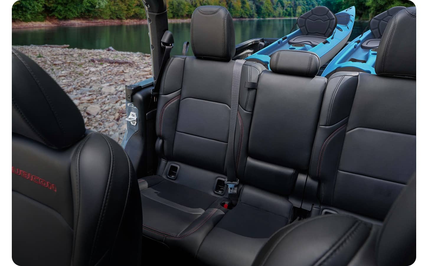 The 2nd row of a 2027 Jeep Gladiator Rubicon with its top and doors off parked on a riverbank. Kayaks can be seen in the truck bed behind the second row.