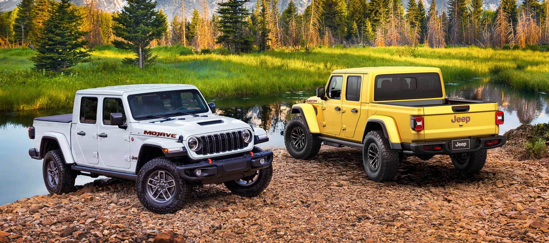 A White 2027 Jeep Gladiator Mojave X and a Hella Yella 2027 Jeep Gladiator Rubicon X parked on a riverbank in the country.