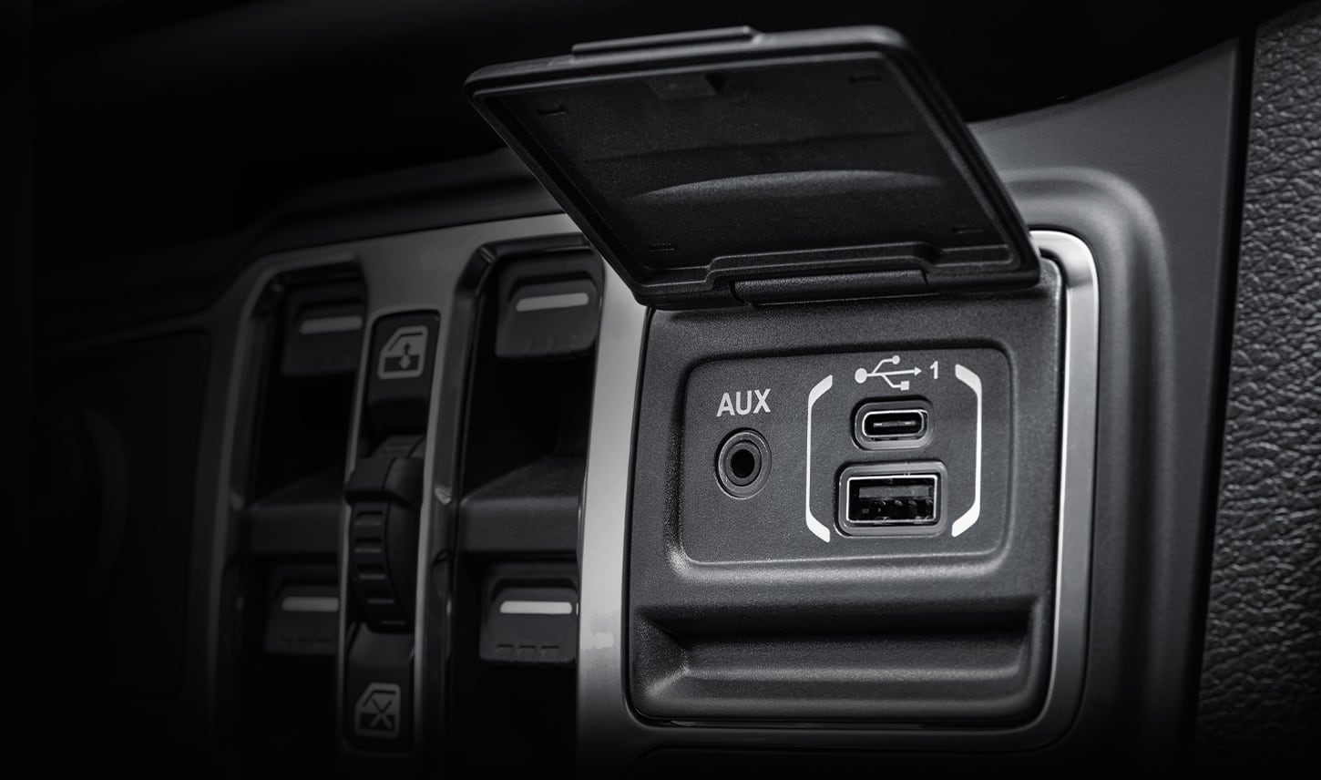 A close-up of the USB and Aux cable plugs on the dashboard of a 2027 Jeep Gladiator.