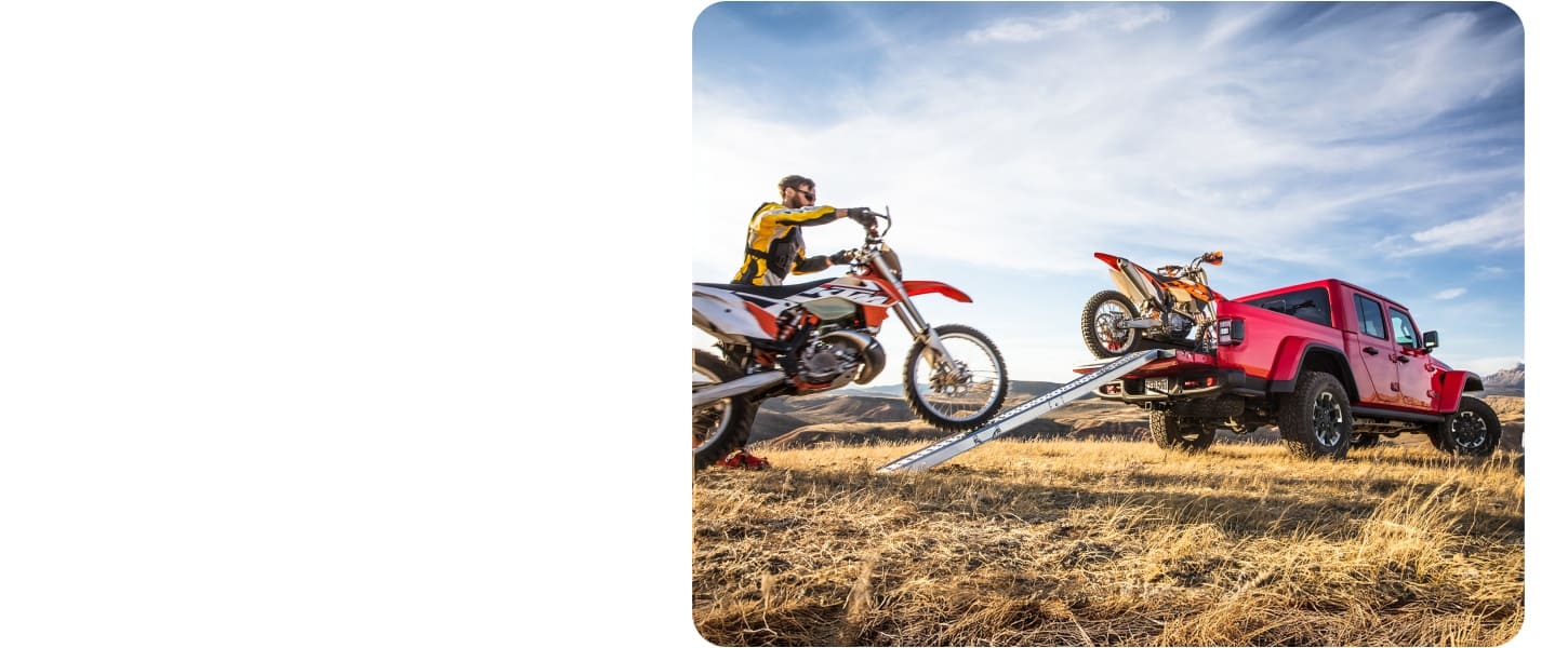 A dirt bike rider rolls his bike up a ramp into the truck bed of a red 2027 Jeep Gladiator.