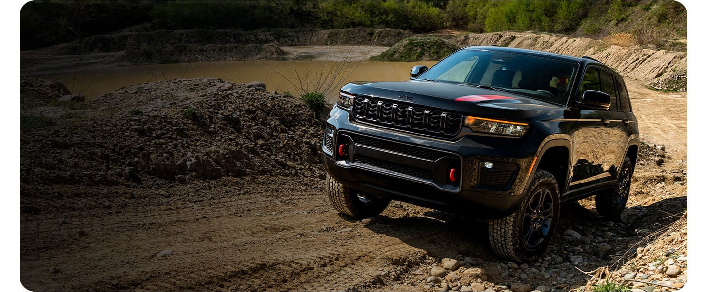A black 2027 Jeep Grand Cherokee Trailhawk ascending a sandy hill off-road.