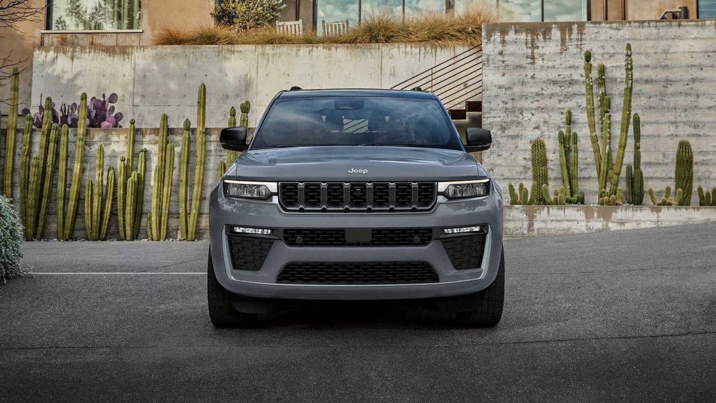 A head-on angle of a gray 2027 Jeep Grand Cherokee Summit parked at a commercial building with a southwestern landscape design.