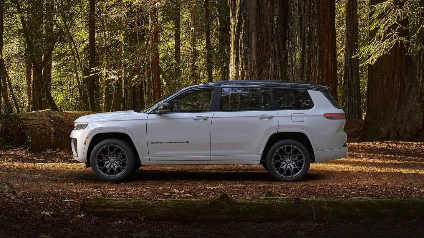 A driver-side profile of a white and black 2027 Jeep Grand Cherokee Summit Obsidian parked in the woods.