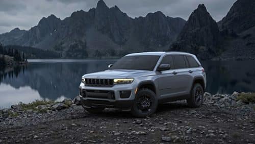  A gray 2027 Jeep Grand Cherokee Upland parked on a rocky beach beside a lake at night.