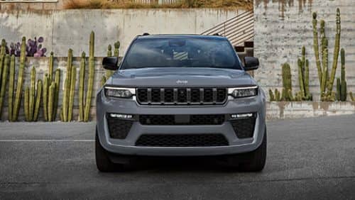 A head-on angle of a gray 2027 Jeep Grand Cherokee Summit parked at a commercial building with a southwestern landscape design.