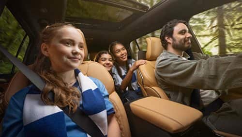 The interior of the 2027 Jeep Grand Cherokee Summit with the male driver and three young female passengers inside--one in the front passenger seat and two in the second row.
