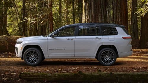 A driver-side profile of a white and black 2027 Jeep Grand Cherokee Summit Obsidian parked in the woods.