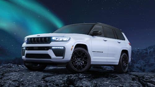 A white and black 2027 Jeep Grand Cherokee Summit Obsidian, parked on a rocky hill at night, with stars and a trail of the northern lights in the background.a