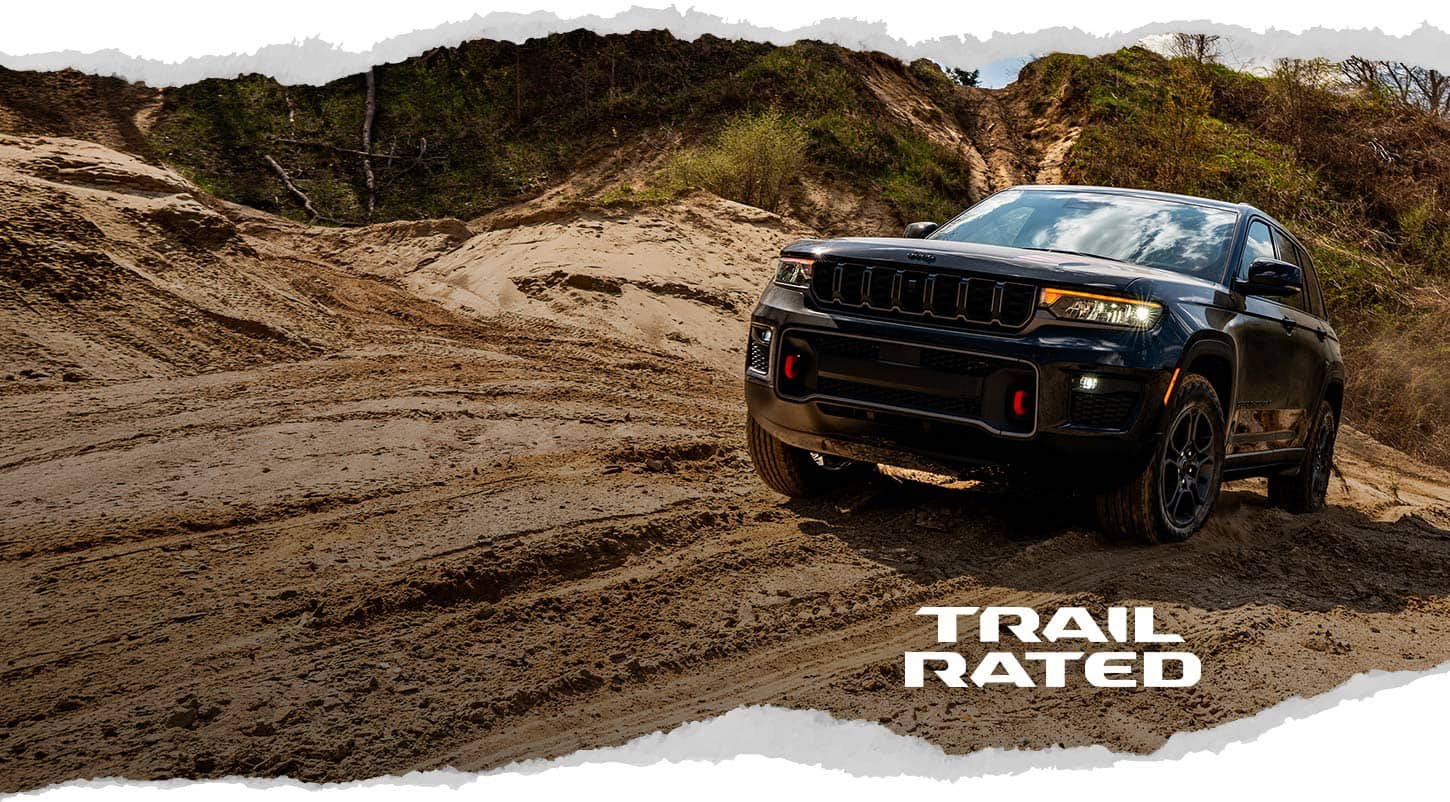 A black 2027 Jeep Grand Cherokee Trailhawk ascending a sandy trail off-road. Trail Rated.