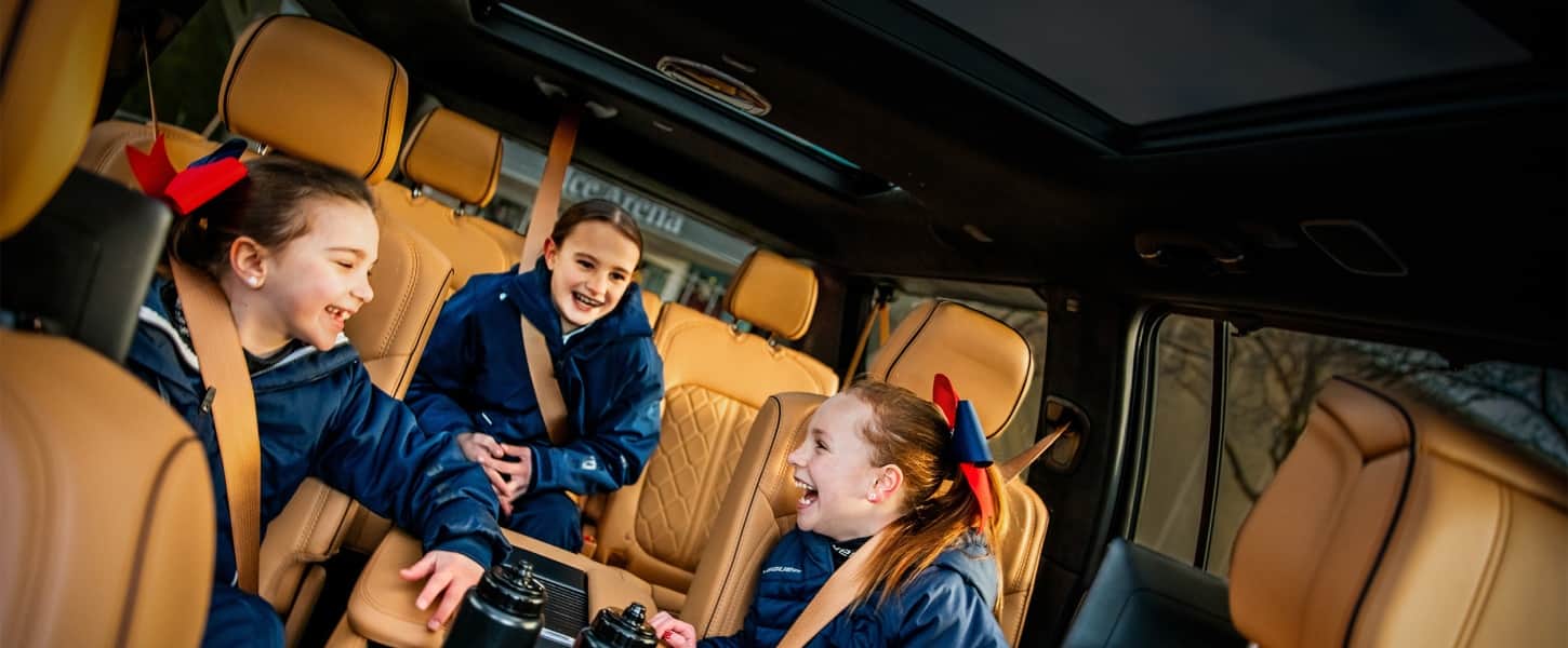 Vista interior del Jeep Grand Wagoneer 2027, donde tres niños están sentados en asientos de cuero tostado y se ríen juntos en la cabina trasera.