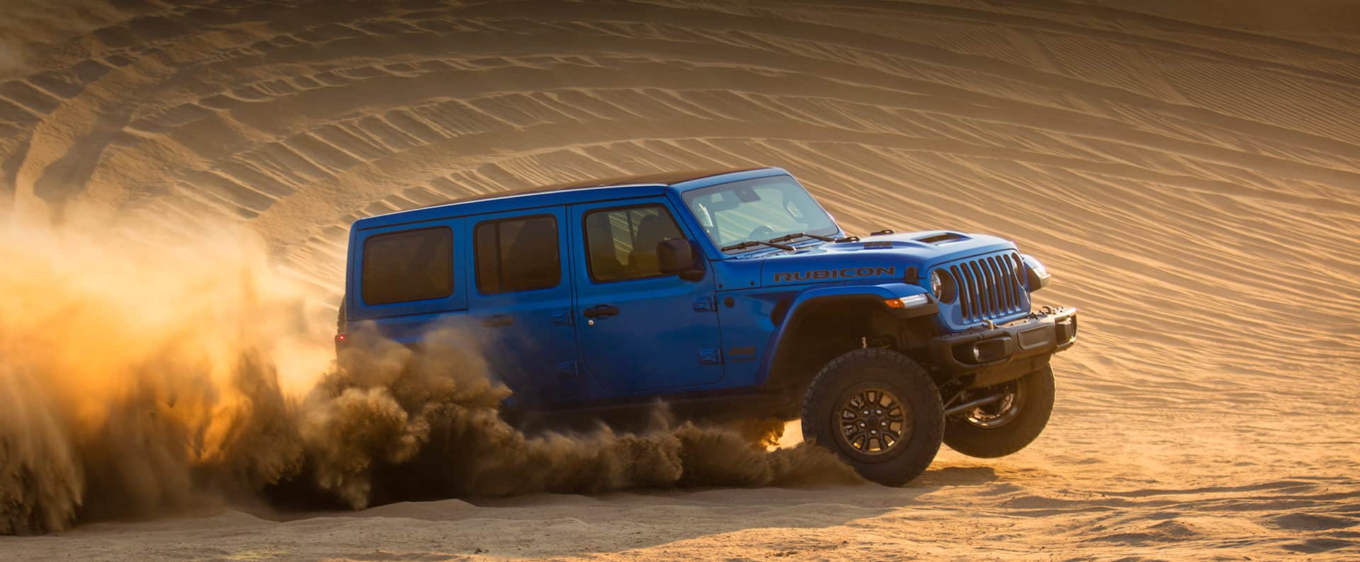 The 2021 Jeep Wrangler Rubicon 392 being driven on a sand dune, a cloud of dust coming from its wheels.