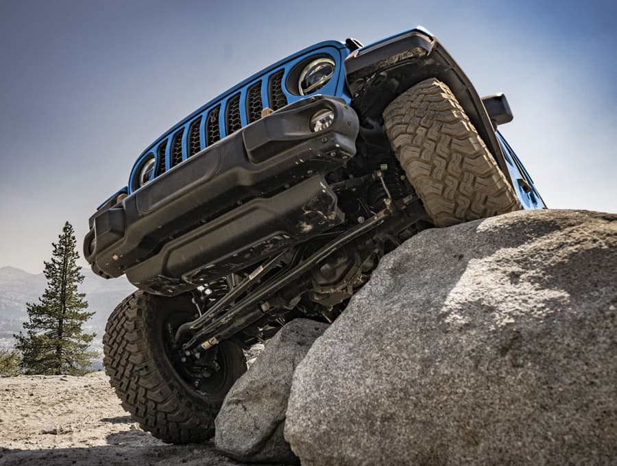 A view from below, of the front axle on the 2021 Jeep Wrangler Rubicon 392, as one wheel climbs a large rock and the other wheel stays on the ground.