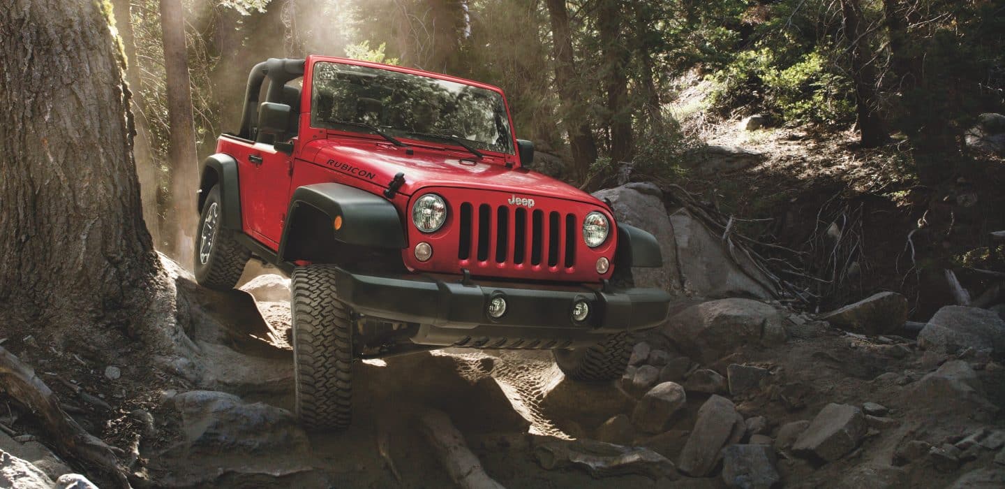 Jeep Wrangler Rubicon being driven on rocky terrain in the forest. 