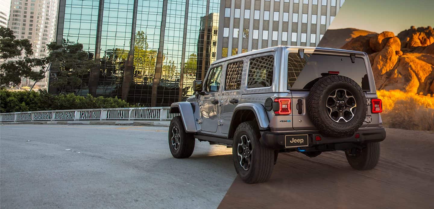Three-quarter rear view of a 2021 Jeep Wrangler 4xe with a split-screen background: skyscrapers on the left, mountains on the right.