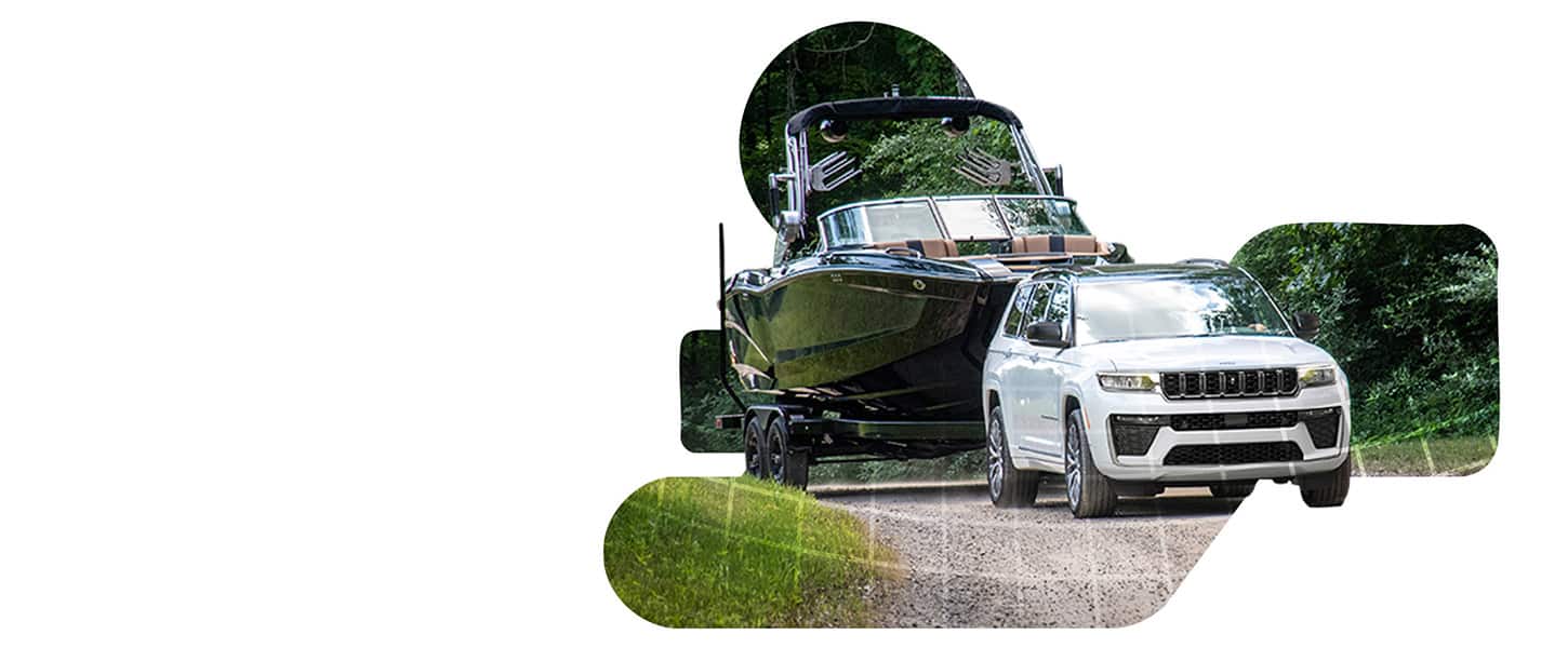 A white 2026 Jeep Grand Cherokee Summit towing a large motorboat down a gravel road.
