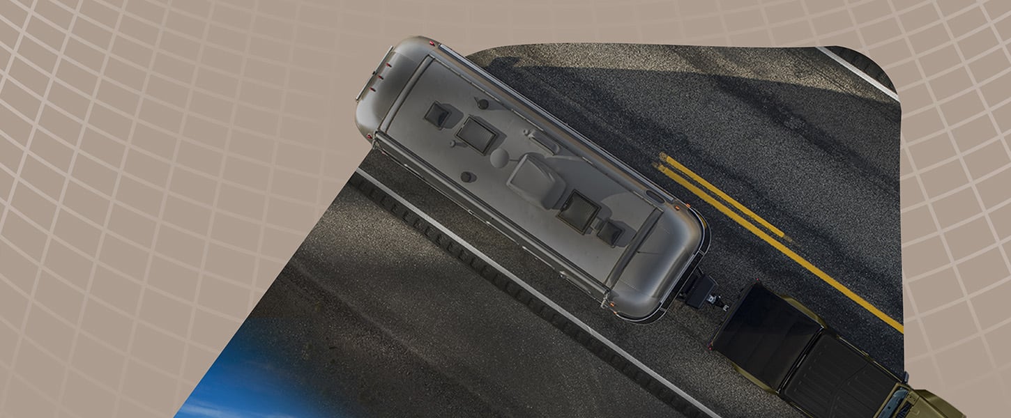 An overhead angle of an olive drab 2026 Jeep Gladiator towing a travel trailer down a highway.