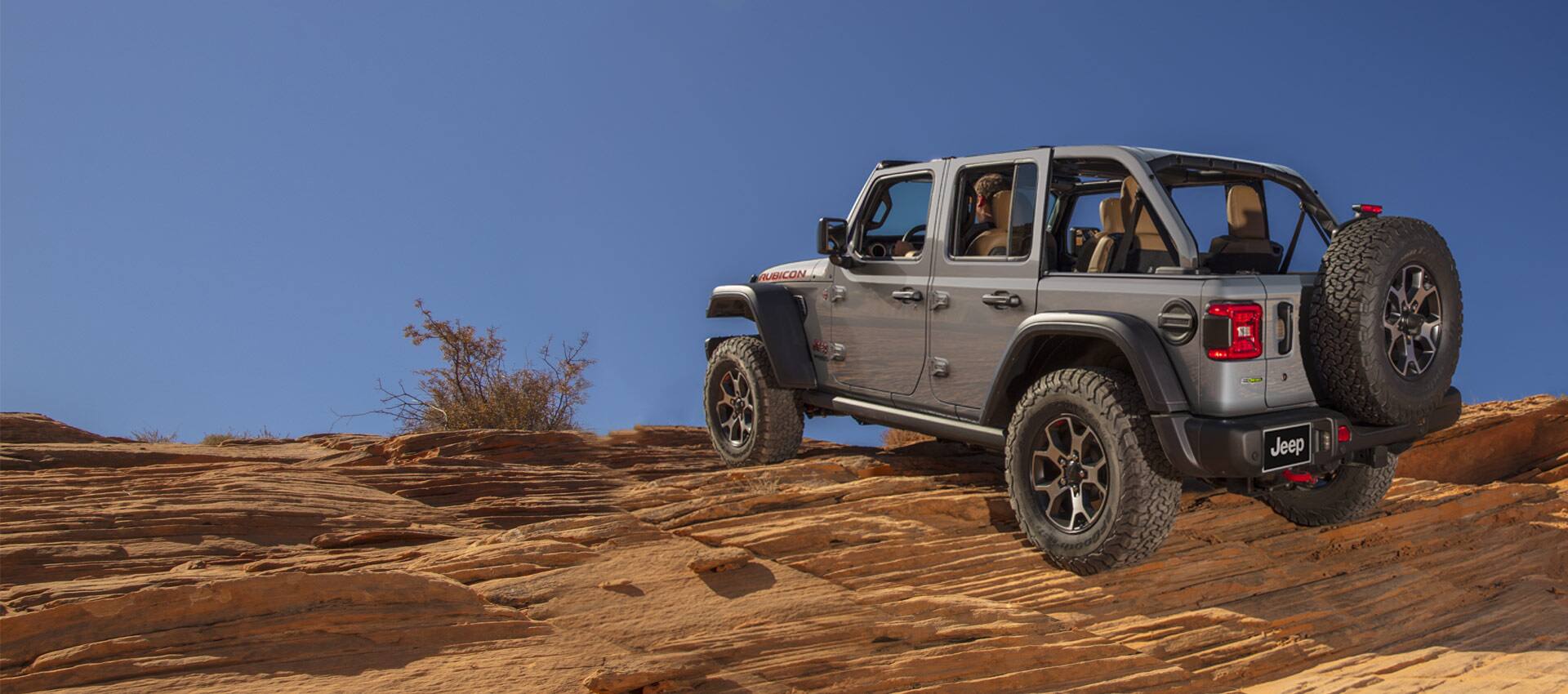 The 2022 Jeep Wrangler Rubicon with its top removed, being driven off-road on a red shale rock formation.
