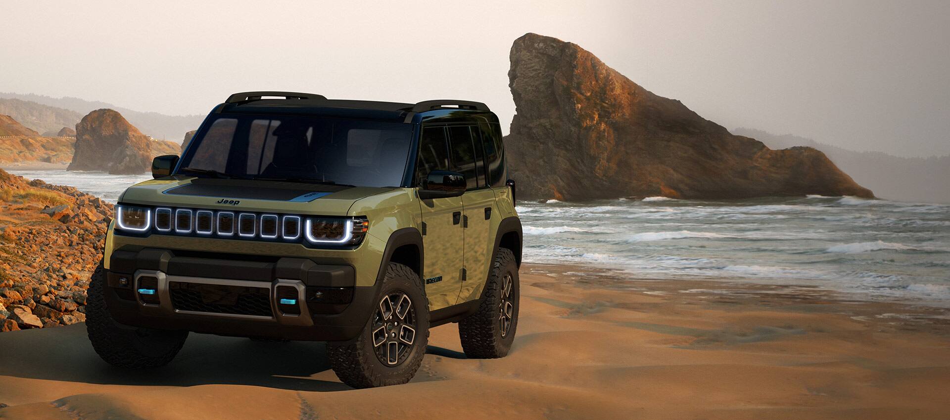 El Jeep Recon 4xe 2023 estacionado en una playa de arena roja con grandes formaciones rocosas a la distancia.