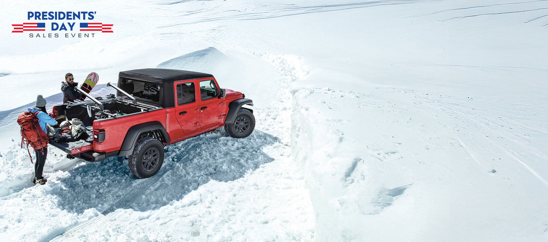 A red 2025 Jeep Gladiator Sport S with black soft top, parked in the snow with a couple removing winter sports equipment from the bed of the truck. The Presidents' Day Sales Event.