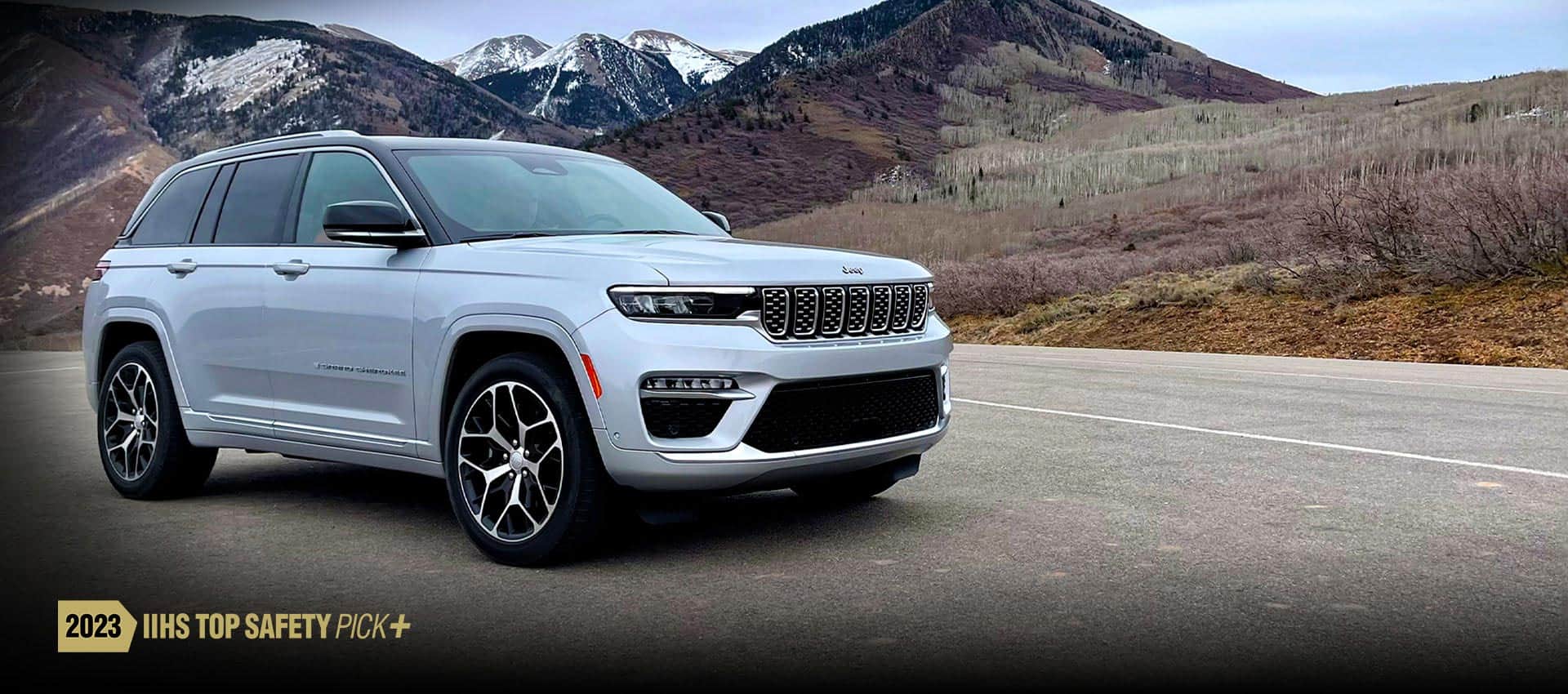 An angled profile of a white 2023 Jeep Grand Cherokee Summit Reserve with a mountain range in the background. The 2023 IIHS Top Safety Pick Plus logo.