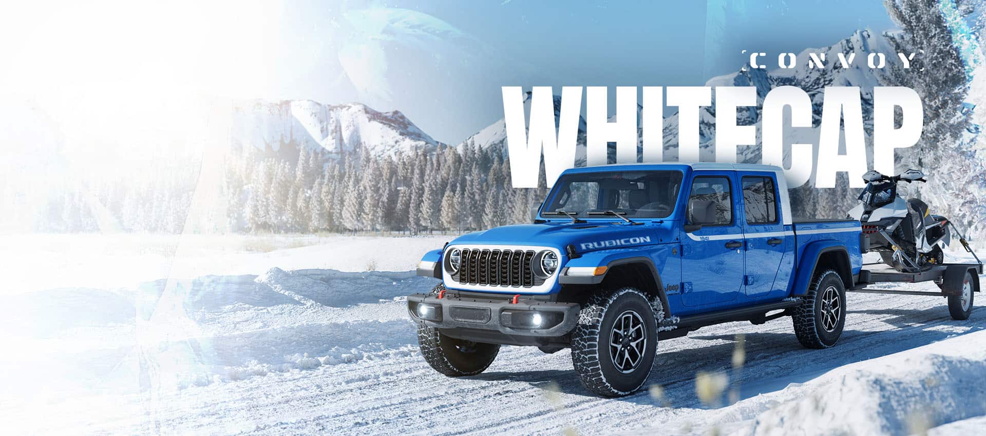 A driver-side front angle of a blue 2026 Jeep Gladiator Rubicon Whitecap traveling on a snow-covered trail, towing an ATV on a flatbed trailer with a forest and mountains in the background. Convoy. Whitecap.