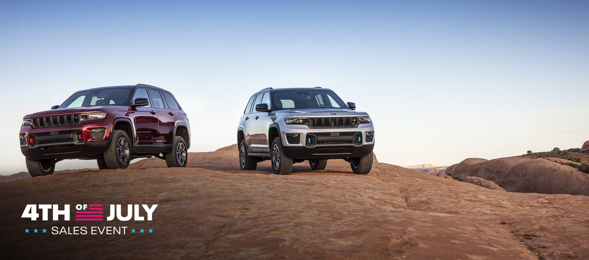 A 2022 Jeep Grand Cherokee Trailhawk and Trailhawk 4xe parked on a rocky plateau. The 4th of July Sales Event Logo.