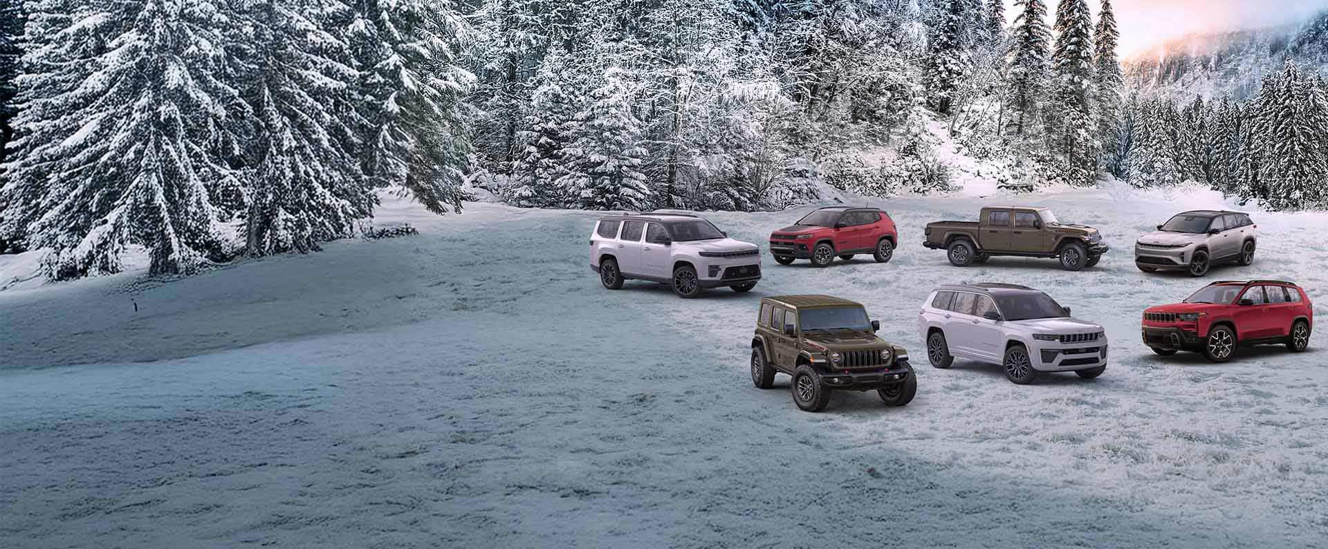 A lineup of seven 2026 Jeep Brand vehicles parked on a snow-covered clearing with a forest in the background. In the front row: an olive drab Wrangler Rubicon X, a white Grand Cherokee Summit and a red Cherokee Overland. In the back row: a white Grand Wagoneer Summit Obsidian, a red Compass Trailhawk, an olive drab Gladiator Mojave X and a silver 2025 Wagoneer S Launch Edition.