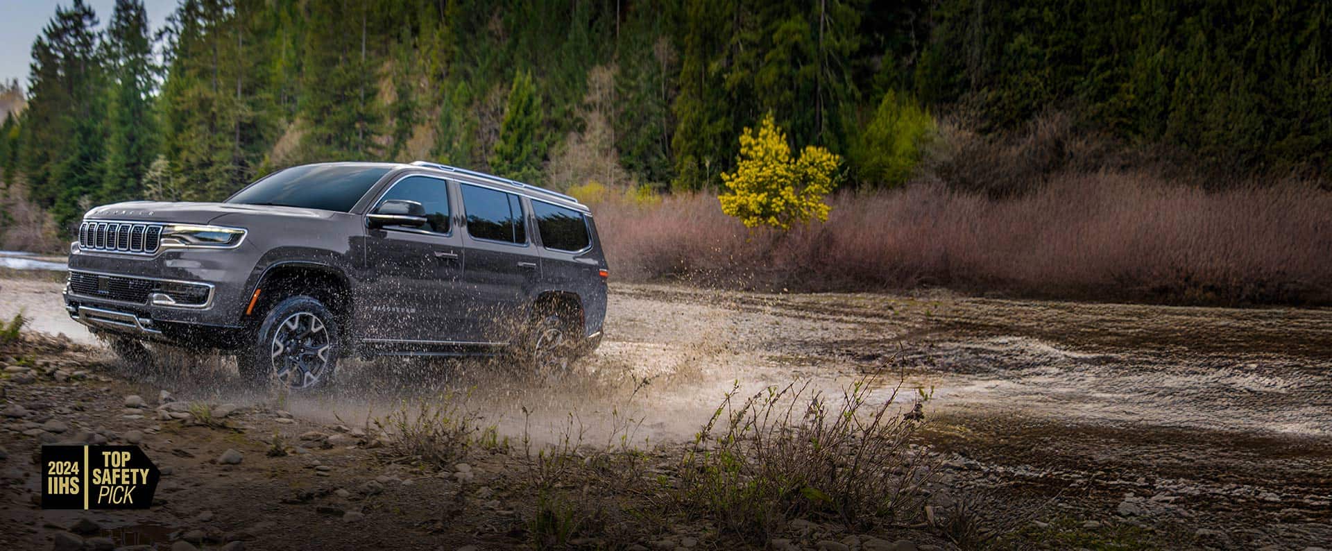 A grey 2024 Grand Wagoneer  L Series 3 exiting a muddy stream off-road. 