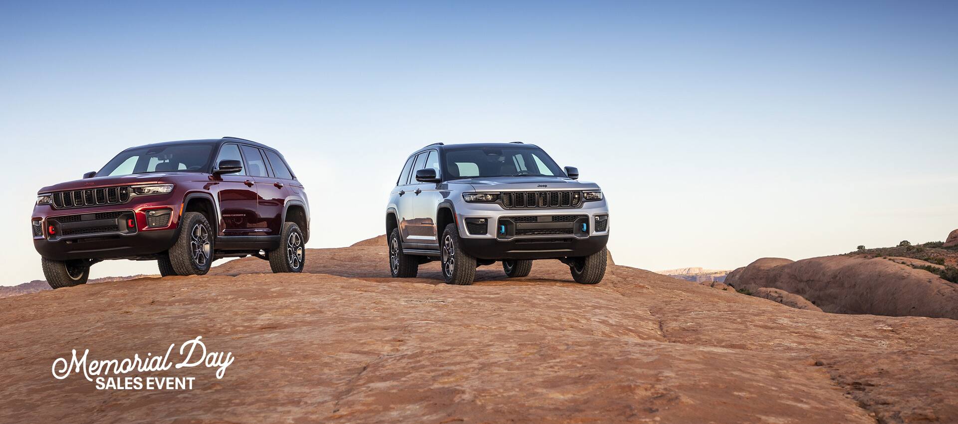 A 2022 Jeep Grand Cherokee Trailhawk and Trailhawk 4xe parked on a rocky plateau. The Memorial Day Sales event logo.